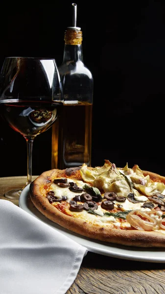 Parma jambonlu pizza, siyah zeytin, mozarella ve sebze, bir bardak kırmızı şarap ve bir şişe zeytinyağı..