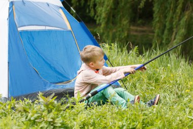 Sevimli küçük çocuk bir çadır bir olta ile onun ellerinde oturur.