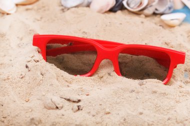 Kum plajı üzerinde kırmızı güneş gözlüğü.