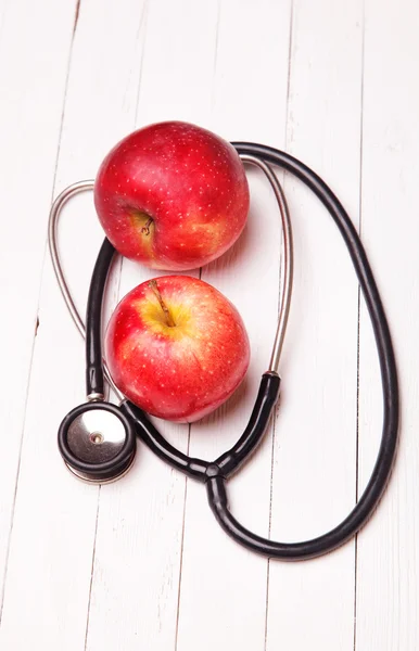 Medical stethoscope and red apple on a white table — Stock Photo, Image