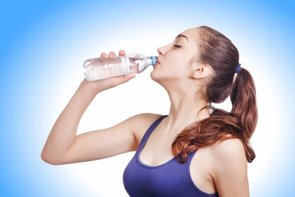 Beautiful athletic girl looks drinks water from a bottle — Stock Photo, Image