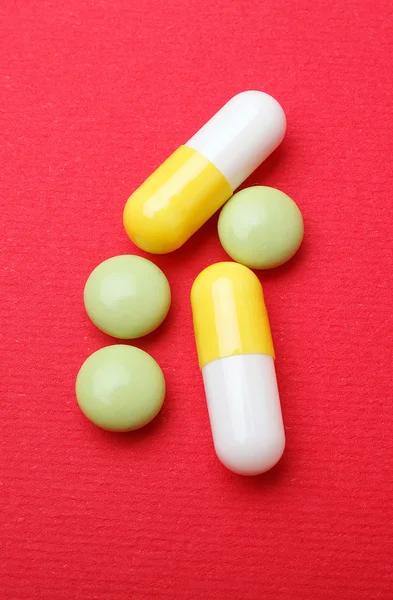 Pil dan kapsul pada latar belakang merah — Stok Foto
