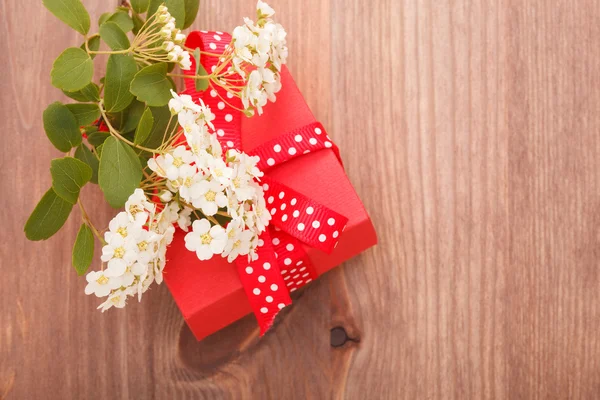 Kırmızı hediye kutusu ahşap arka plan üzerinde kırmızı kurdele ve çiçekler bağlı — Stok fotoğraf