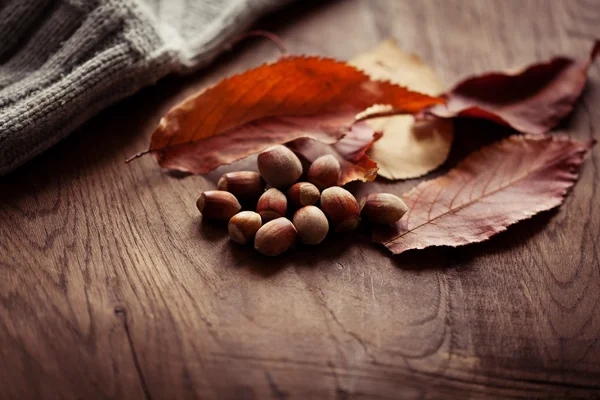 Avellanas con hojas de otoño en el fondo de una tabla de madera —  Fotos de Stock