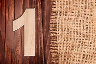Wooden digit one symbol - 1. On wooden table background wih burlap clipart