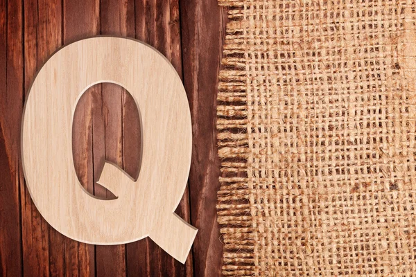 Wooden alphabet letter symbol - Q. On wooden table background wih burlap — Stock Photo, Image