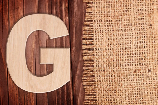Letra del alfabeto de madera símbolo - G. Sobre fondo de tabla de madera wih arpillera — Foto de Stock