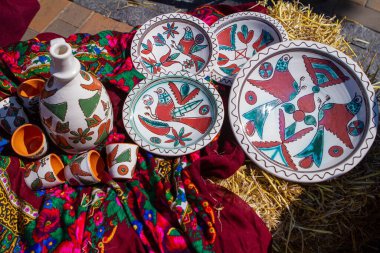 El yapımı ve el boyalı sığ çorba seramik tabaklar geleneksel Podillia özeti ve kırmızı havluda kuş desenleri, masa olarak saman yığını, Ukrayna geleneksel folklor sembolik sanatı
