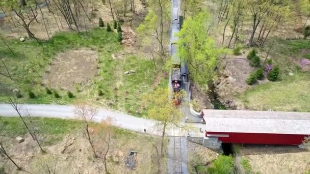 1860年代の蒸気旅客列車が森の中を旅している様子を空中から眺めるロンリー シングル レール ロード トラックに屋根付きの橋を渡る — ストック動画