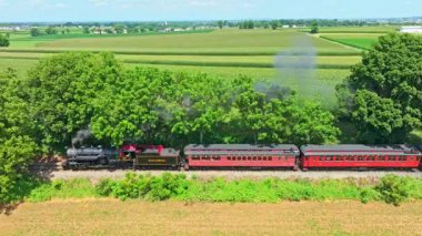 Paradise, Pennsylvania, 8-8-2025 - A steam train travels along a railway surrounded by vibrant green fields and trees under a clear sky. The countrysides beauty enhances the nostalgic experience of