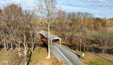 Etrafı yapraksız ağaçlarla çevrili dolambaçlı bir yolda kırsal bir köprü manzarası. Parlak mavi gökyüzü, ilkbaharın başlarındaki topraksı tonlara katıksız bir tezat sağlar..