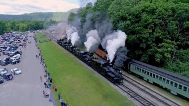 Cass, Batı Virginia, 18-2022 tarihsel bir buhar treni raylar boyunca seyahat ediyor ve dumanlar salıyor. Seyirciler otlak alanda toplanarak bu nostaljik deneyimin tadını çıkarıyorlar.