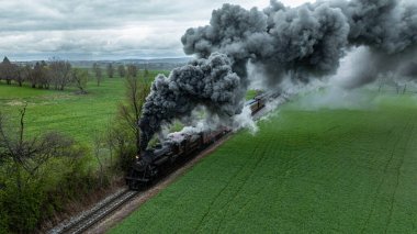 Cennet, Pennsylvania, 12 Nisan 2025 - Bir buhar makinesi yeşil alanlar boyunca hareket ediyor. Trenden yükselen yoğun duman ağaçların ve açık arazinin yanından geçiyor..