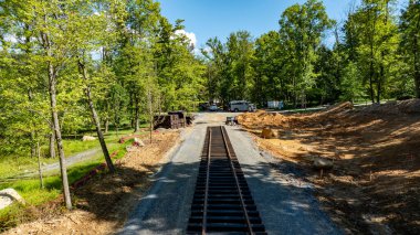 İşçiler ormanlık bir alanda yeni demiryolu rayları döşüyorlar. İnşaat malzemeleri yakınlarda düzenlenirken, etrafındaki ağaçlar gölge sağlıyor. Proje daha başlangıç aşamasında..