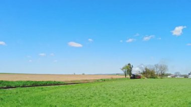 Cennet, Pensilvanya, 22 Nisan 2024 - Bir buhar treni açık alanlarda yol alıyor. Trenin dumanı tüterken güneş gökyüzünde parlıyor. Çevresindeki tarlalar ağaçlarla yeşildir.