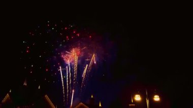 Toplum kutlamaları sırasında evlerin üzerinde havai fişekler patlarken parlak renkler gökyüzünü aydınlatıyor. İnsanlar renkli gösteriyi heyecan ve neşeyle izlemek için toplanıyor..