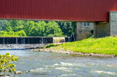 Kırsal bir bölgede kırmızı kaplı bir köprünün altından sular akar. Kenarlarından su damlayan küçük bir baraj görülebilir. Sahneyi çevreleyen yeşil ağaçlar ve çimenler basit ve doğal bir manzara yaratıyor..