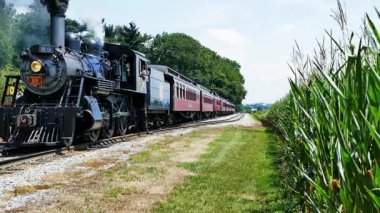 Cennet, Pennsylvania, 2 Ağustos 2024 - Yolcular buharlı tren yolculuğunun tadını çıkarıyorlar. Tren raylar boyunca hareket eder, duman bırakır. Aileler trenin geçişini izlemek için toplanır.