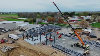 Gordonville, Pennsylvania, 9 Nisan 2025 - Vinçler kırsal alanda yeni bir yapı inşa etmek için çalışıyorlar. Makineler çelik çerçeveleri kaldırırken işçiler ekipmanları inşaat alanında gezdiriyorlar. Site şu an meşgul.
