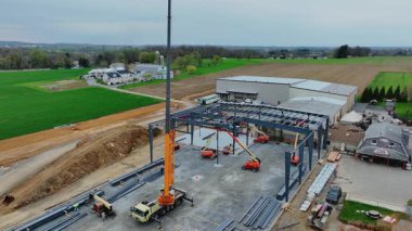 Gordonville, Pennsylvania, 9 Nisan 2025 - İşçiler ve makineler kırsal alanda yeni bir yapı inşa ediyorlar. Büyük bir vinç çelik kirişleri kaldırırken, ekipler de asansörleri ve kamyonları çalıştırıyor.