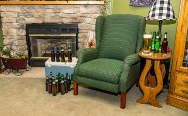 Gordonville, Pennsylvania, 10 Haziran 2025 - Oturma odasındaki taş şöminenin yanında yeşil bir sandalye oturuyor. Birkaç şişe küçük bir masaya ve sandalyenin etrafına yerleştirilir. Sahnenin rahatlatıcı bir havası var.