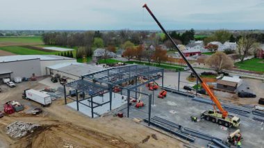 Gordonville, Pennsylvania, 9 Nisan 2025 - İşçiler açık bir alanda metal bir yapı oluşturmak için vinç kullanıyorlar. Kamyon ve makineler olay yerinde. Mekan kırsal alanların karışımını gösteriyor.