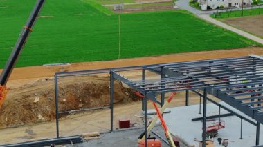 Gordonville, Pennsylvania, 9 Nisan 2025 - İşçiler kırsal kesimdeki bir inşaat alanında meşguller. Bir vinç yeni bir binanın çerçevesini oluşturmak için çelik kirişleri kaldırır. Alanı çevreleyen yeşil alanlar