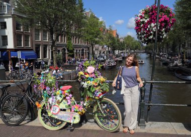 Amsterdam, Hollanda - 11 Ağustos 2017: Kız, Hollanda 'nın tarihi Amsterdam kentinde 11 Ağustos 2017 tarihinde bir kanalda bir köprüde çiçeklerle süslenmiş bir bisikletin yanında poz veriyor