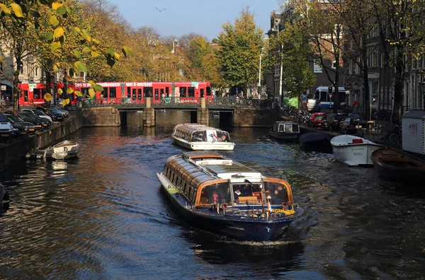 荷兰阿姆斯特丹 2016年11月11日 2016年11月11日 在荷兰阿姆斯特丹 当一辆红色电车在一条长满秋树的运河上行驶时 人们乘船游览 — 图库照片
