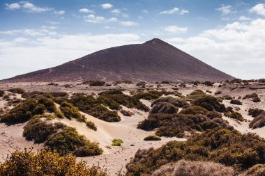 İspanya 'nın Kanarya Adaları, Tenerife, El Medano yakınlarındaki Doğal Montana Roja volkanik manzarası. Altın kum tepeleri ve dramatik volkanik dağ Atlantik kıyısında çarpıcı bir çöl manzarası yaratır. Hiki ile bilinen korunan doğal alan.