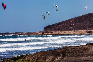 El Medano, Tenerife, Kanarya Adaları, İspanya 1 Mart 2026: Atlantik kıyısındaki Montana Roja volkanik dağı yakınlarında dalgalarda sörf yapan uçurtma sörfçüleri. El Medano plajı Kanarya Adası 'nın en ünlü uçurtma ve rüzgar sörfü merkezlerinden biridir.