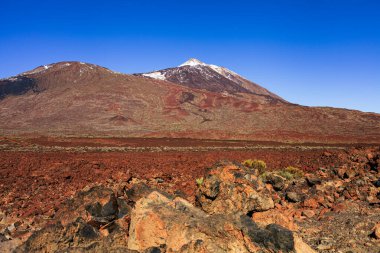 Teide Dağı 'nın muhteşem manzarası Teide Ulusal Parkı, Tenerife, Kanarya Adaları, İspanya' daki kırmızı volkanik lav sahasının üzerinde yükseliyor. Renkli kayalar, lav oluşumları ve berrak mavi gökyüzü ile dramatik volkanik manzara en büyük