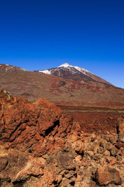 Teide Dağı 'nın muhteşem manzarası Teide Ulusal Parkı, Tenerife, Kanarya Adaları, İspanya' daki kırmızı volkanik lav sahasının üzerinde yükseliyor. Renkli kayalar, lav oluşumları ve berrak mavi gökyüzü ile dramatik volkanik manzara en büyük