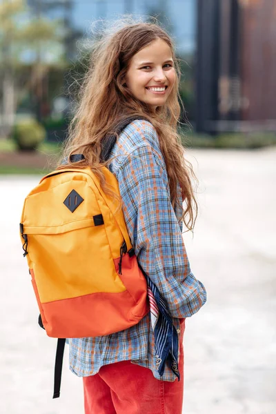Atrakcyjna młoda blondynka hipsterka student z plecakiem patrząc wstecz do kamery ze szczęśliwą twarzą. — Zdjęcie stockowe