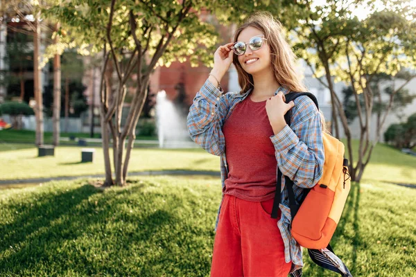 Alegre joven rubia hipster mujer estudiante con mochila mirando hacia otro lado con cara feliz. — Foto de Stock