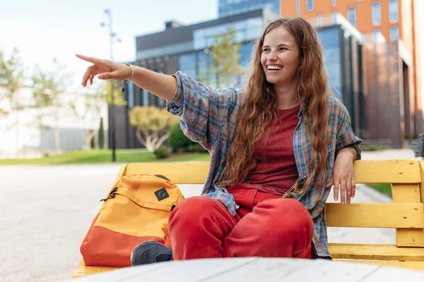 Smiling young blonde hipster woman student with backpack pointing finger away at university. — Stock Photo, Image