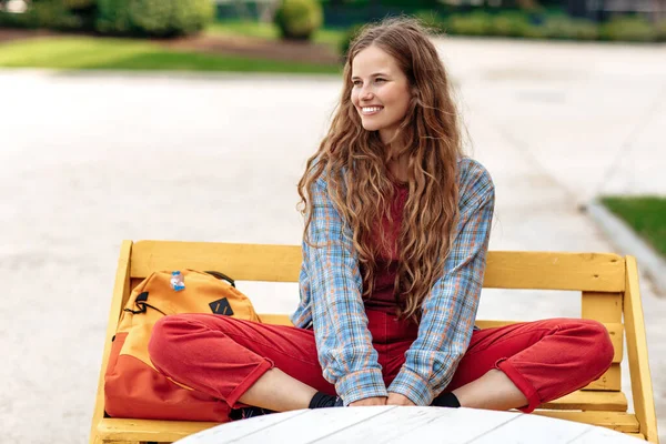 Sırt çantalı çekici sarışın hippi kız öğrenci üniversitede bankta oturuyor.. — Stok fotoğraf