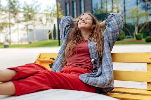 Atractiva joven rubia hipster mujer estudiante con mochila buscando relajarse en el banco en la universidad. — Foto de Stock