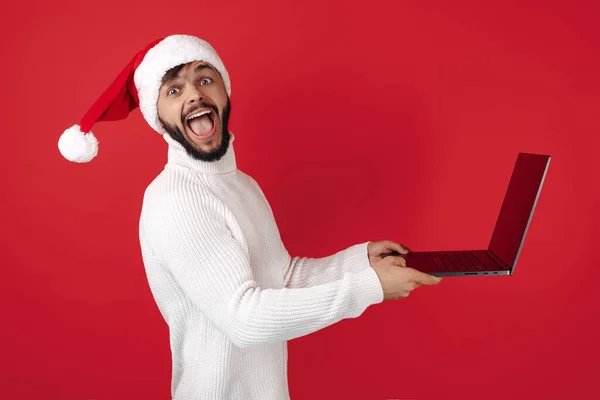 Homem hipster feliz usa chapéu de Papai Noel usando notebook sobre fundo vermelho. Conceito de Natal e Ano Novo. — Fotografia de Stock
