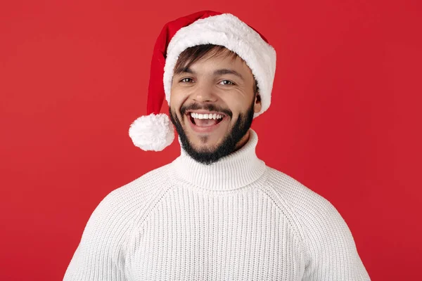 Homem hipster sorrindo usa chapéu de Papai Noel sobre fundo vermelho. Conceito de Natal e Ano Novo. — Fotografia de Stock