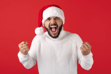 Kendine güvenen hippi, Noel Baba şapkası takıyor ve başarıyı kırmızı arka planda kutluyor. Noel ve Yeni Yıl kavramı.