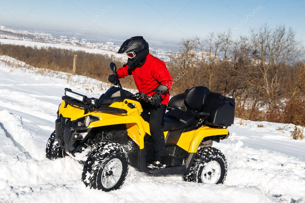 Extremal driver driving his ATV quad bike stand in heavy snow with deep wheel track.