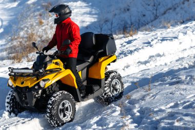 ATV bisikletli genç adam, yoğun kar altında, derin tekerlek yolu ile ayakta duruyor. Moto kış sporları.