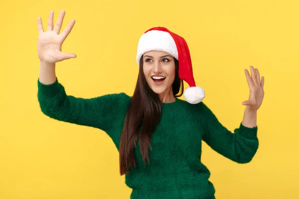 Jovem morena alegre usa chapéu de Papai Noel e pulôver verde sobre fundo amarelo. — Fotografia de Stock