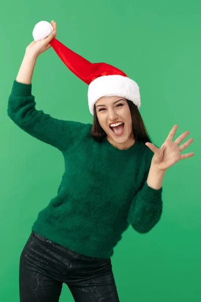 Jovem morena alegre usa chapéu de Papai Noel e pulôver verde sobre fundo verde. — Fotografia de Stock