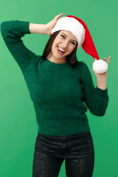 Feliz jovem morena usar chapéu de Papai Noel e pulôver verde sobre fundo verde. — Fotografia de Stock