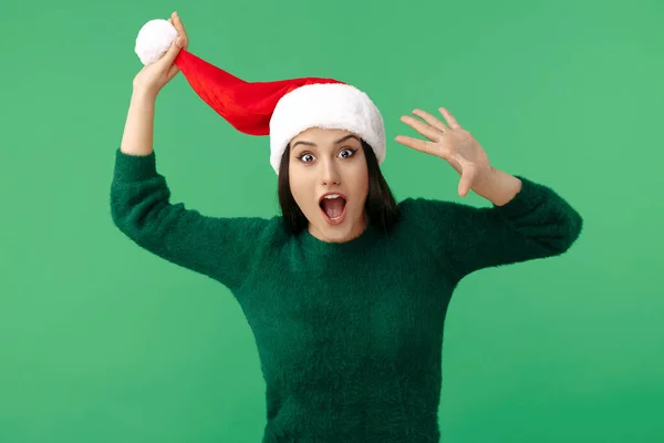 Fantastiska unga brunett kvinna bära Santa claus hatt och ull pullover peka finger bort över grön bakgrund. — Stockfoto