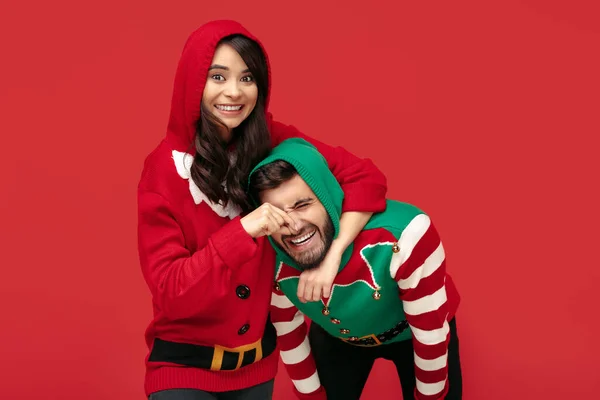Glada par klädd i jul roliga tröjor som har kul över röd bakgrund. — Stockfoto