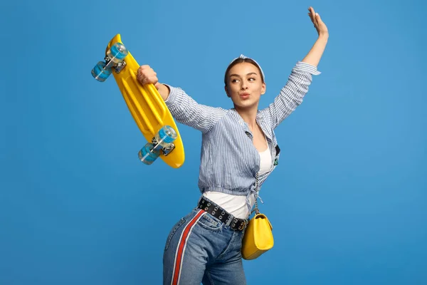 Snygg ung kvinna med gul penny eller skateboard över blå bakgrund. — Stockfoto