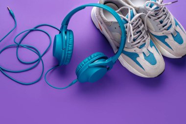 Mor arka planda modern mavi kulaklık ve spor ayakkabılar. Müzik konsepti.